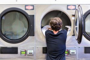 A laundromat worker removing linens from an industrial laundry machine.