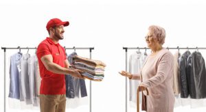 A man in a red uniform delivering folded clothes to an elderly woman.