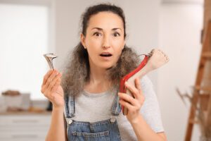 A woman with a surprised look on her face holds a broken high heel in her hands.
